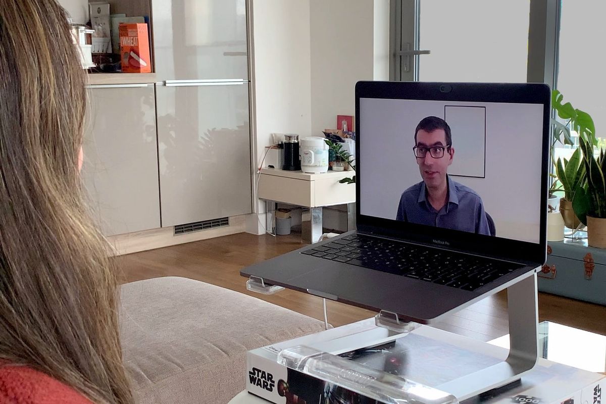 A communication coach appears via Zoom on a laptop screen in an apartment